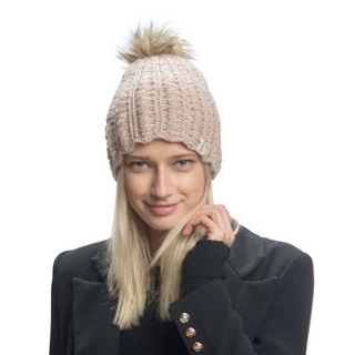 Sentence with product name: A woman with blonde hair wearing a light-colored Layla Beanie with a scallop knit pattern and a pom-pom on top, handmade in Nepal, and a black coat, smiling at the crowd.