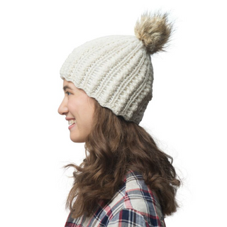 A person in a white Layla Beanie with a scallop knit pattern and a pompom, smiling and looking to the side.
