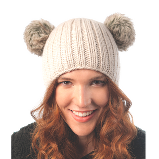 A smiling woman with red hair wearing a Double Pom Beanie with faux fur poms.