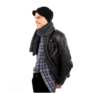 A person wearing a black leather jacket, a gray scarf, and a Knit Jockey Cap, smiling and looking to the side against a white background.