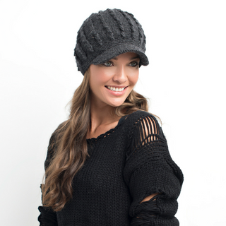 A smiling woman with long hair wearing a black handmade Nepal wool Knit Jockey Cap and a black sweater with a distressed shoulder detail.