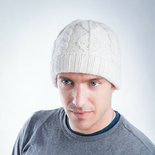 A man with blue eyes wearing a white Leaf Pattern Cap w/ Rib Fold made in Nepal merino wool beanie and a gray t-shirt, looking slightly to the side.
