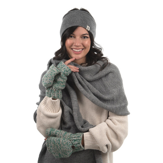 A woman is smiling and posing for the camera, wearing winter accessories that include a grey beanie, Bedford Fingerless Gloves with flap handmade in Nepal, and a large grey scarf over a cream-colored sweater.