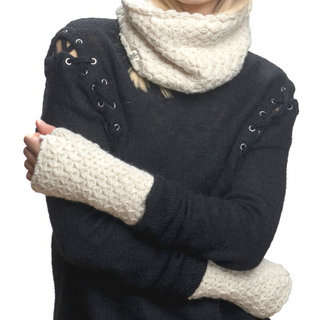 A person wearing a black I See Stars Merino Handwarmers sweater with lace-up details on the sleeves and a white knit scarf, standing with their arms crossed.