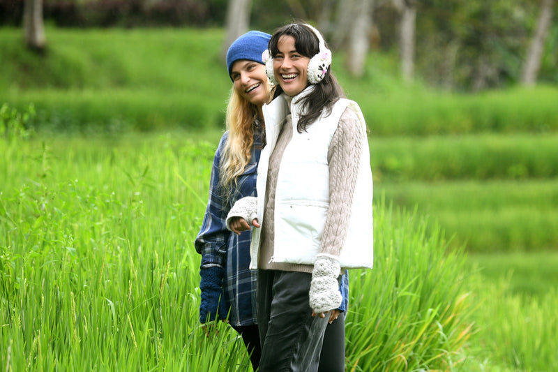Two friends laughing in a rice field, one in bunny earmuffs