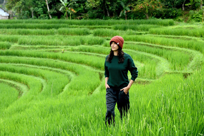 Woman in a rust knit beanie walking through green rice terraces