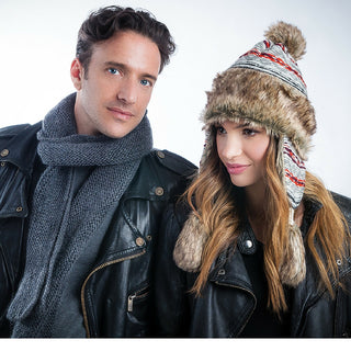 A man and a woman wearing winter attire, including leather jackets and hats, pose for a photograph. The man has a Marbled Scarf around his neck, and the woman is wearing a knit beanie.