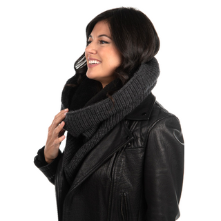 A woman wearing a black leather jacket and a dark Mick Neckwarmer smiles while looking to the side.