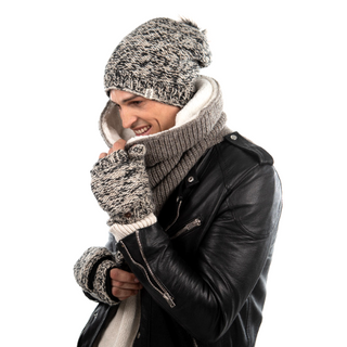A person wearing a handmade in Nepal knit hat, Mick Neckwarmer, and gloves, bundled up in winter clothing made from merino wool, and smiling slightly while looking to the side.