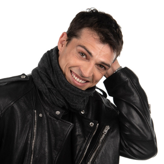 A smiling man in a black leather jacket and a Branch Out Neckwarmer leaning on his hand against a white background.