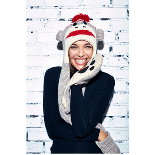 A woman is smiling brightly at the camera while wearing a Cute Monkey Hatscarf with long sides that could be used as a scarf and mittens, all hand-knit from Merino Wool.