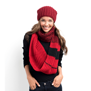 A smiling woman wearing a red Ivy League Infinity Scarf and hat, handmade in Nepal, paired with a black sweater, standing against a white background.