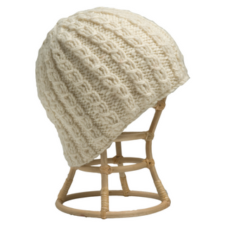 A cream-colored Small Chain Knit Beanie cap, displayed on a wooden stand.