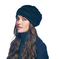 A woman with long brown hair wears the Hand Loom Branch Out Slouch, a black handmade wool beanie, paired with a dark turtleneck sweater. She looks slightly to the side with a neutral expression against a white background.