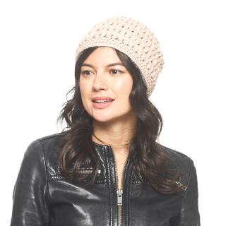 A woman wearing a light pink, merino wool Good Vibes Beanie handmade in Nepal and a black leather jacket.