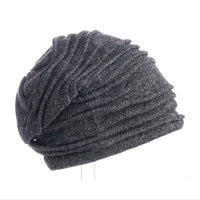 The Hand Loom Branch Out Slouch is displayed on a white background, positioned sideways to highlight its dark gray, ribbed knit wool design and slouchy silhouette. This handmade beanie provides both warmth and distinctive style for cooler days.