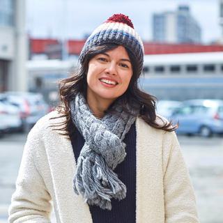 A smiling woman wearing a winter hat and a handmade Oslo Scarf from Nepal outdoors.