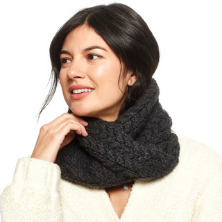 A woman with dark hair wearing a black Dream On Neckwarmer and a cream-colored top looks away from the camera with a thoughtful expression.